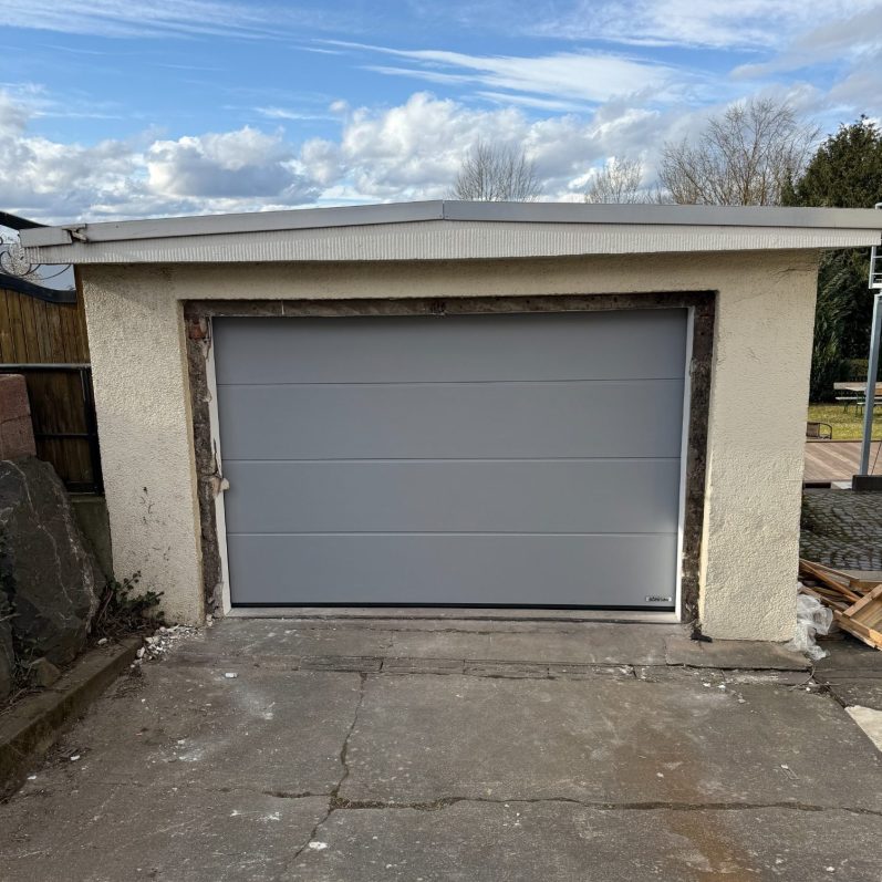 Zu sehen ist ein Hörmann Sektionaltor L-Sicke Planar Farbe CH9006 Weiß - Aluminium Matt